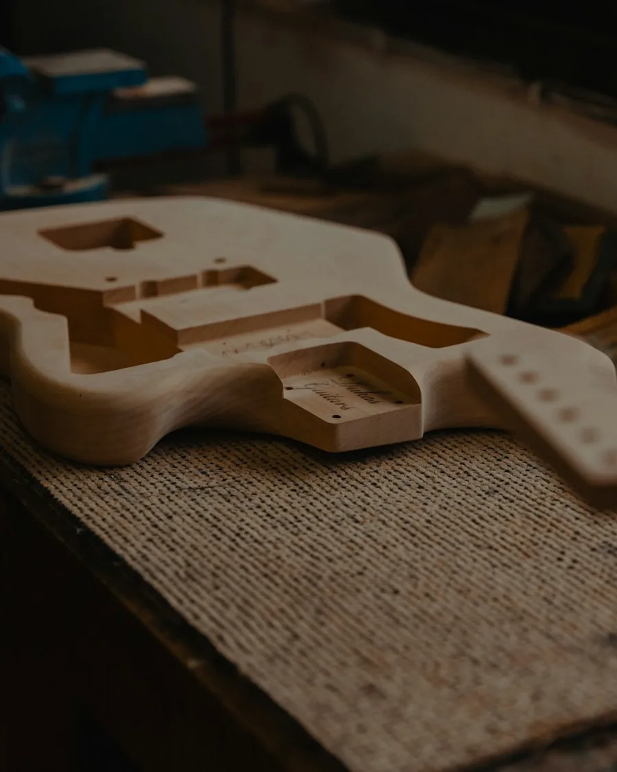 Cuerpo de guitarra ya perfilado y fresado, con el alojamiento del mástil visible, apoyado sobre el banco de un taller